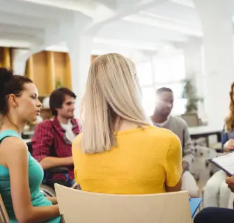 Eine gemischte Gruppe junger Menschen sitzen im Kreis und diskutieren miteinander.