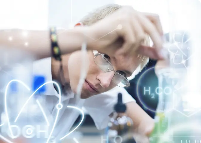 Junger Student bei einem Chemie-Experiment. Im Vordergrund sieht man einige Formeln über das Bild laufen.