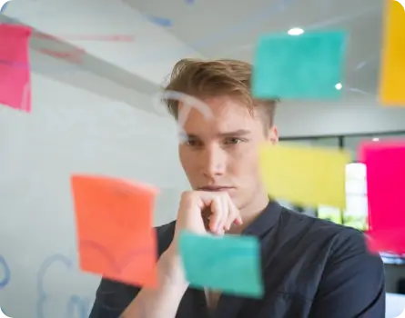TMS Vorbereitung – junger Mann grübelt vor einer Scheibe an der Post-Its hängen und Notizen geschrieben stehen.