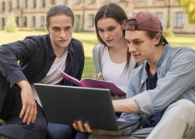 Zwei Studenten und eine Studentin schauen gemeinsam auf ein Laptop. Sie informieren sich über das Medizinstudium an privaten Unis