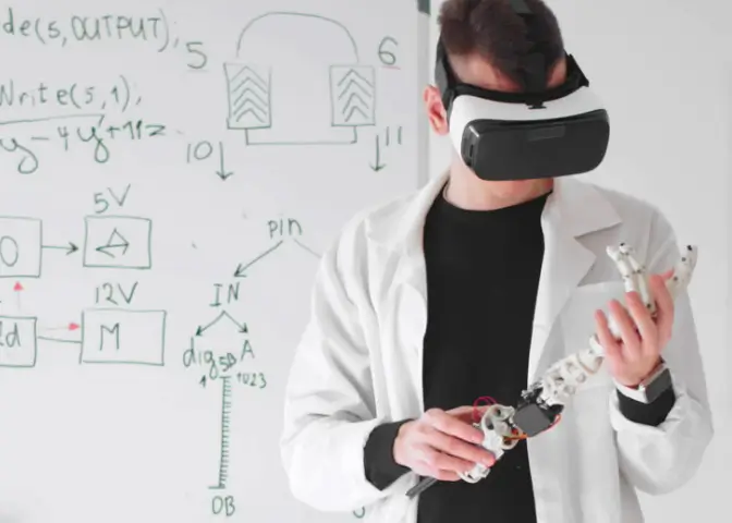 Physik Vertiefung –wissenschaftlicher Mitarbeiter blickt durch die VR-Brille. In seiner Hand hat er eine Roboterarmprothese