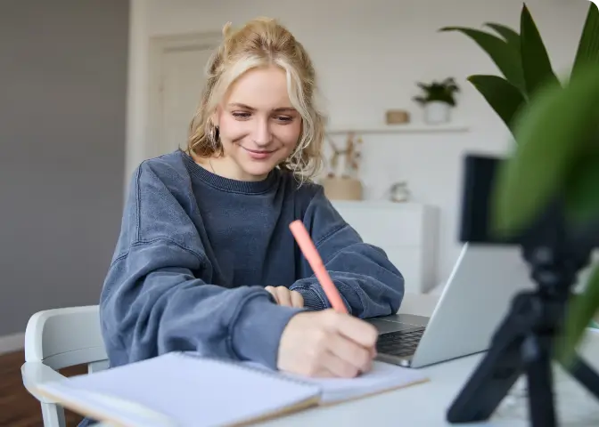 TMS Vertiefung – zufriedene junge Frau sitzt vor ihrem Laptop und schreibt Notizen