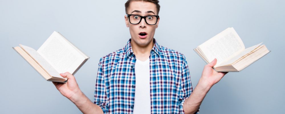 Portrait of confused stylish handsome attractive nice trendy caucasian guy, wearing casual checkered shirt and glasses, holding two books, isolated over light grey background